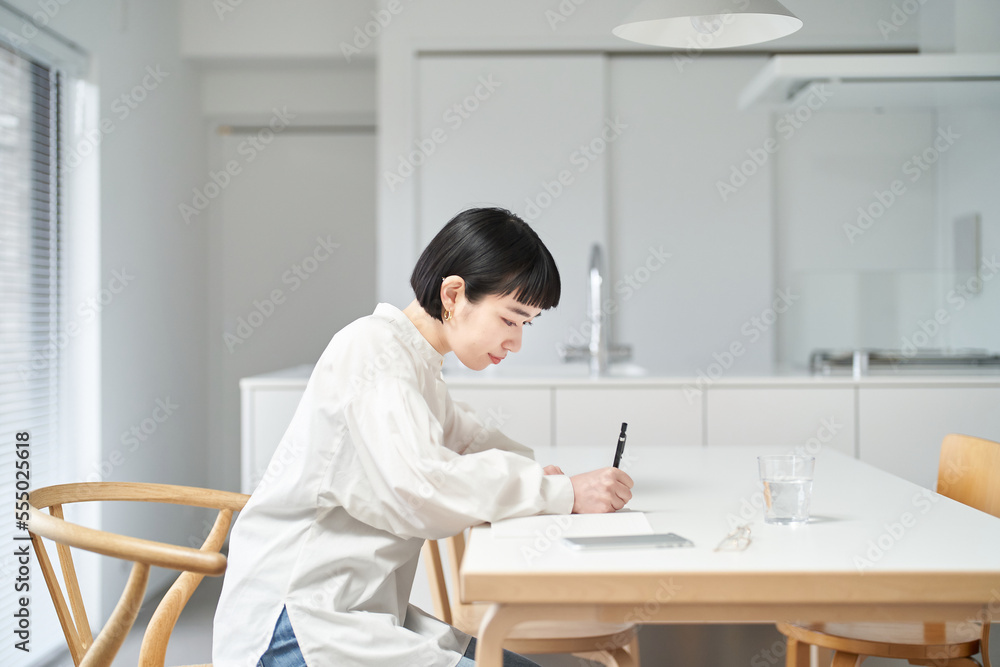 部屋でノートに書きものをする若い女性 部屋でノートに書きものをする若い女性