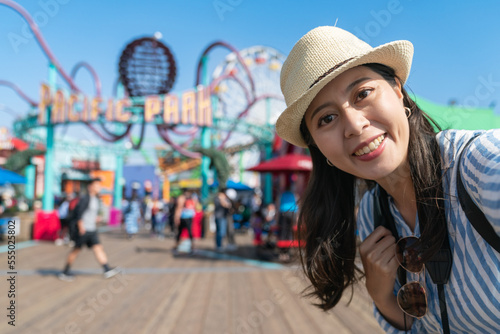 closeup self portrait of happy asian Chinese woman visitor at amusement park of santa monica pier. she is looking at camera on blurred background of the entry of fairground