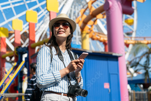 portrait of cheerful asian Taiwanese girl backpacker wearing sunglasses exploring in amusement park using travel guide on phone on ferris wheel background