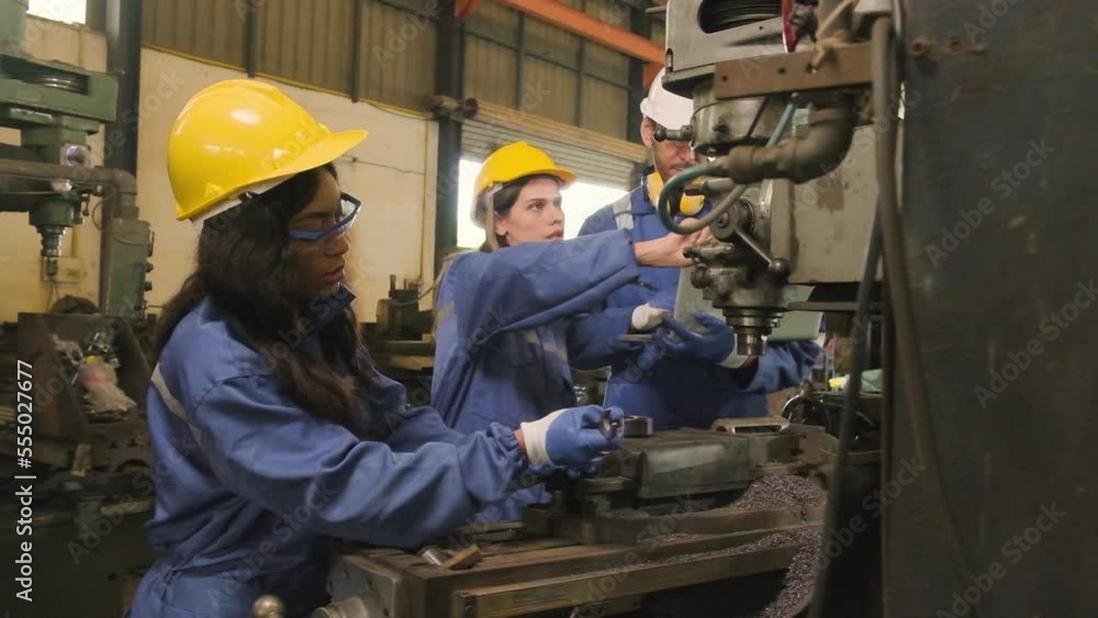 An Industrial workers team in protective and safety uniforms and hardhats, male manager, and female colleagues work with metalwork machines in manufacturing factory. Professional production engineer. An Industrial workers team in protective and safety uniforms and hardhats, male manager, and female colleagues work with metalwork machines in manufacturing factory. Professional production engineer.