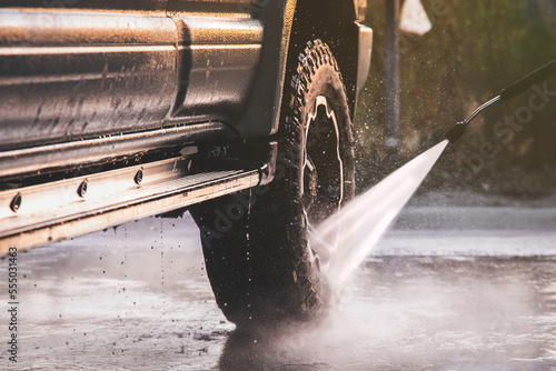 Washing offroader car at a self-service car wash with a high-pressure water jet after off-road driving.
