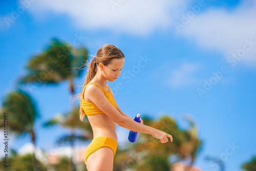 Adorable teen girl in yellow bikini applying sunscreen cream on the beach photo