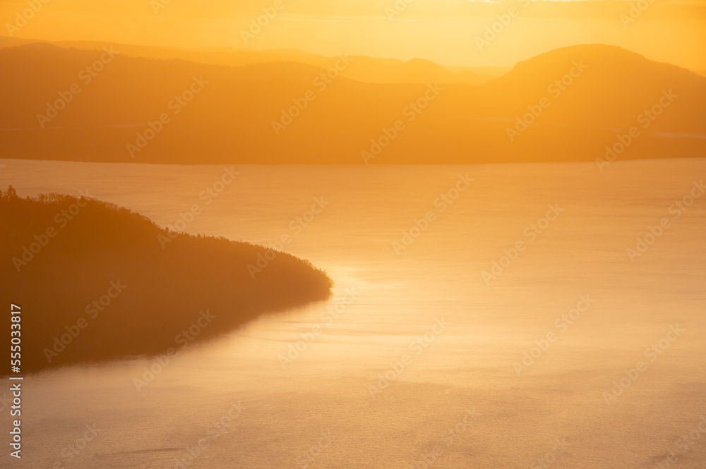 眩しい太陽光にオレンジ色に霞む湖と山。