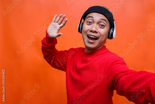 POV of joyful influencer with headphones and listening to music while taking selfie isolated on orange background.