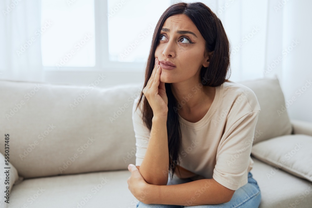 Woman toothache, tooth root inflammation sitting on sofa at home Woman toothache, tooth root inflammation sitting on sofa at home