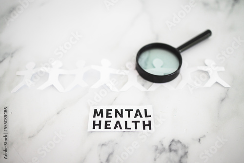 Menatal health text next to paper people chain with magnifying glass on one person,  psychology and need for help photo