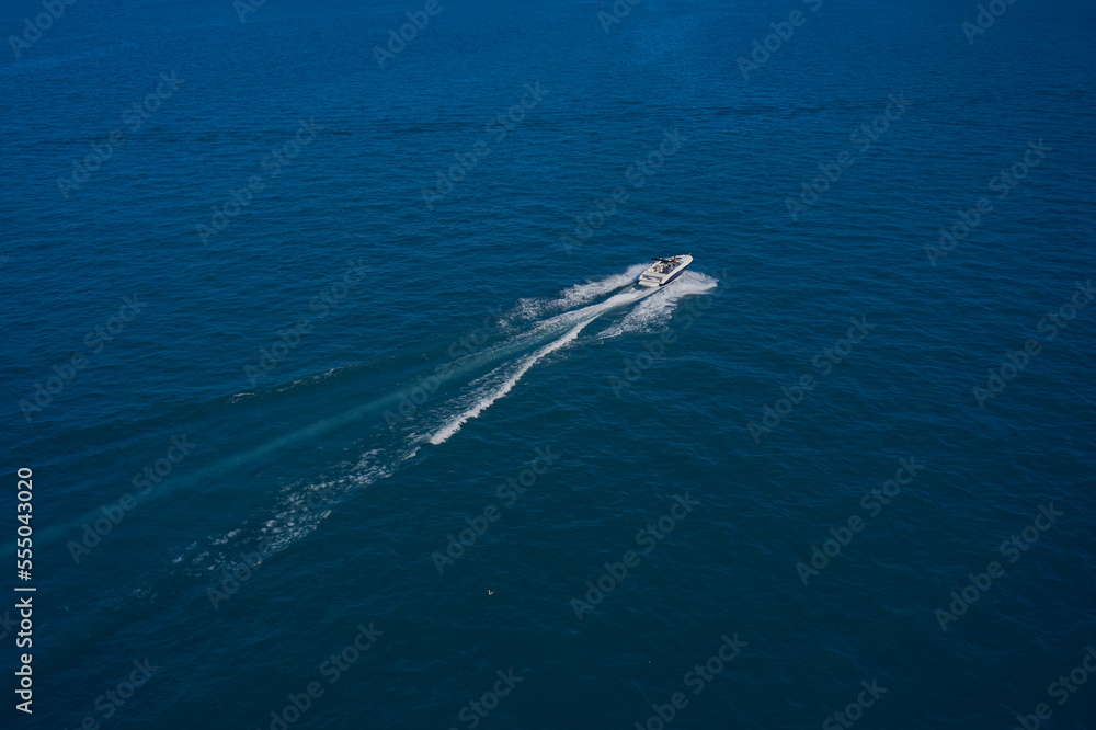 A boat with a motor on blue water. Top view of a white boat sailing in the blue sea. Top view of the boat. Aerial view luxury motor boat. A boat with a motor on blue water. Top view of a white boat sailing in the blue sea. Top view of the boat. Aerial view luxury motor boat.