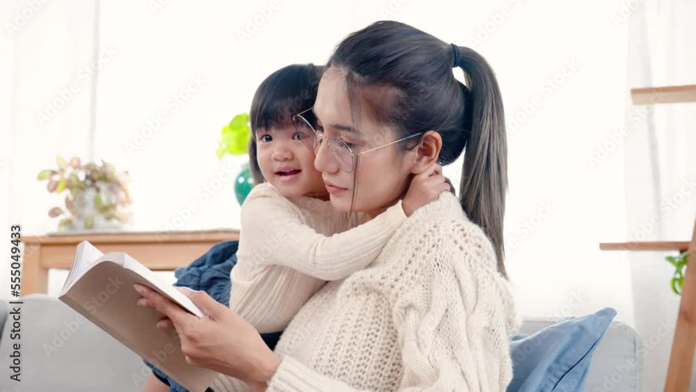 4K, Pregnant Asian single mom reading book comfortably on sofa in living room of her home with her daughter standing and hugging her with her, two seemed very close and loved each other very much. 4K, Pregnant Asian single mom reading book comfortably on sofa in living room of her home with her daughter standing and hugging her with her, two seemed very close and loved each other very much.