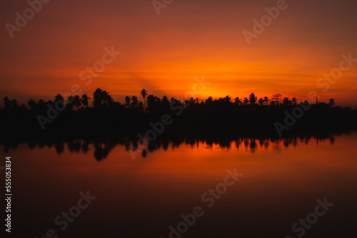 Orange sunset and sky reflection in water with silhouette of trees.  Natural background and texture.