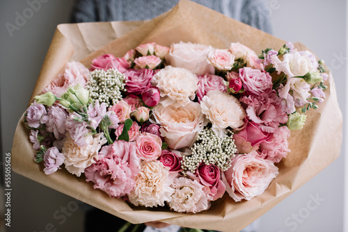 a young woman holding luxurious, huge and beautiful bouquet of fresh roses, carnations, eustoma, matthiola flowers in tender pink colors, cropped photo, bouquet close up