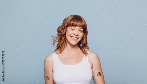 Obraz na plátně Young, cheerful woman with ginger hair stands in a studio setting, wearing a tank top and smiling at the camera