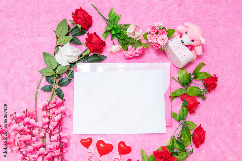 White blank A4 paper on the to of pink envelope surrounded by valentine themed decorations White blank A4 paper on the to of pink envelope surrounded by valentine themed decorations