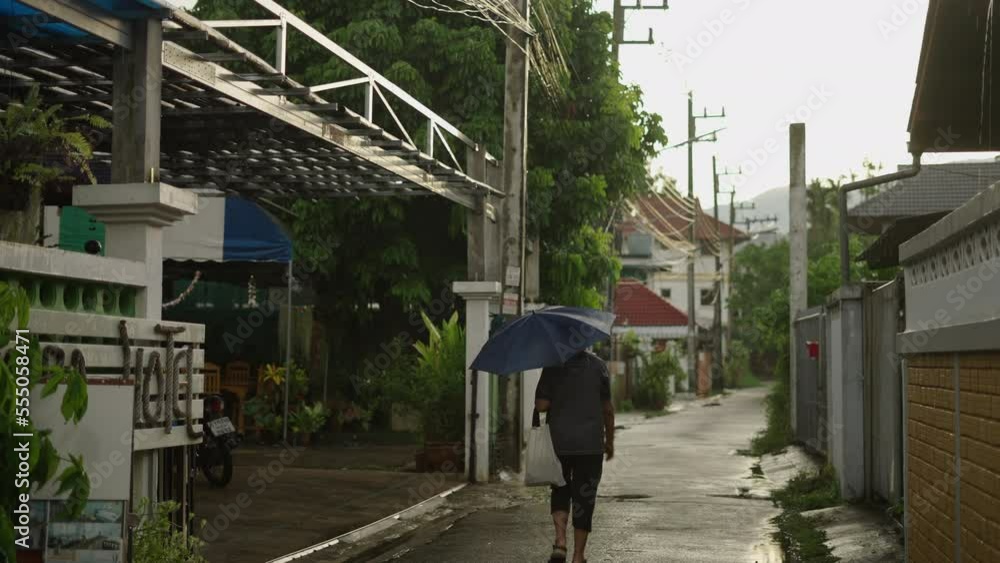 Elderly man walking with a bag and umbrella on a street in Chiang Mai Elderly man walking with a bag and umbrella on a street in Chiang Mai