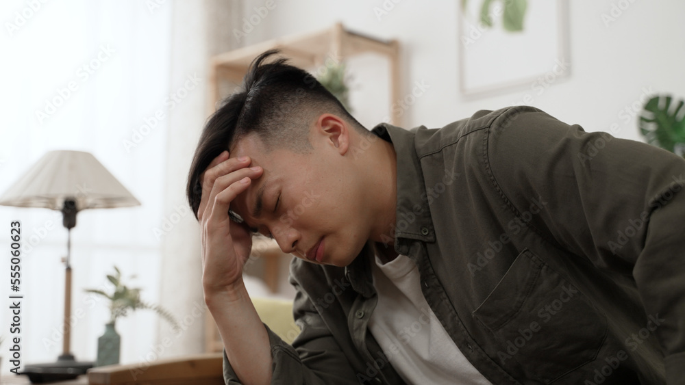 closeup shot of a stressed asian young male staying at home is propping head in despair while feeling great anxiety about financial problems during lockdown. closeup shot of a stressed asian young male staying at home is propping head in despair while feeling great anxiety about financial problems during lockdown.