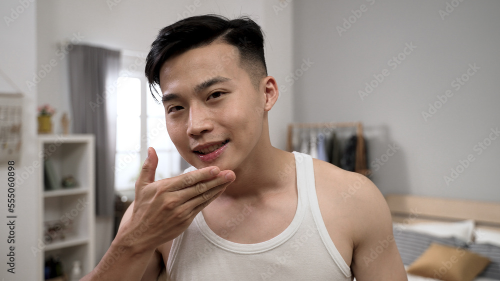 handsome asian young guy look at the camera as mirror and touching his smooth face skin with smile during morning beauty routine at home. handsome asian young guy look at the camera as mirror and touching his smooth face skin with smile during morning beauty routine at home.