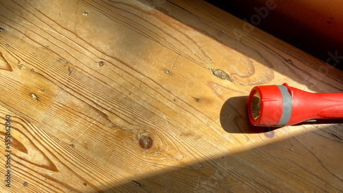 A red small flashlight on wooden table. Sunlight resembles the light from a flashlight. photo