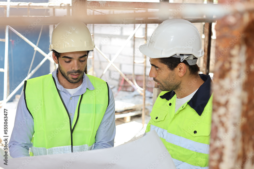 Two technician civil engineer or specialist inspector discussing, brainstorm and planing work with laptop, blueprint and walkie talkie radio together at Industrial building site. Construction concept Two technician civil engineer or specialist inspector discussing, brainstorm and planing work with laptop, blueprint and walkie talkie radio together at Industrial building site. Construction concept