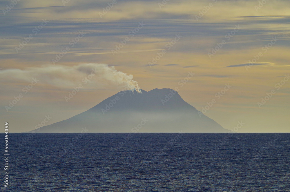 Stromboli volcano at horizon with clouds of smoke coming from summit seen from outdoor deck of luxury cruiseship cruise ship liner during Mediterranean cruising at twilight