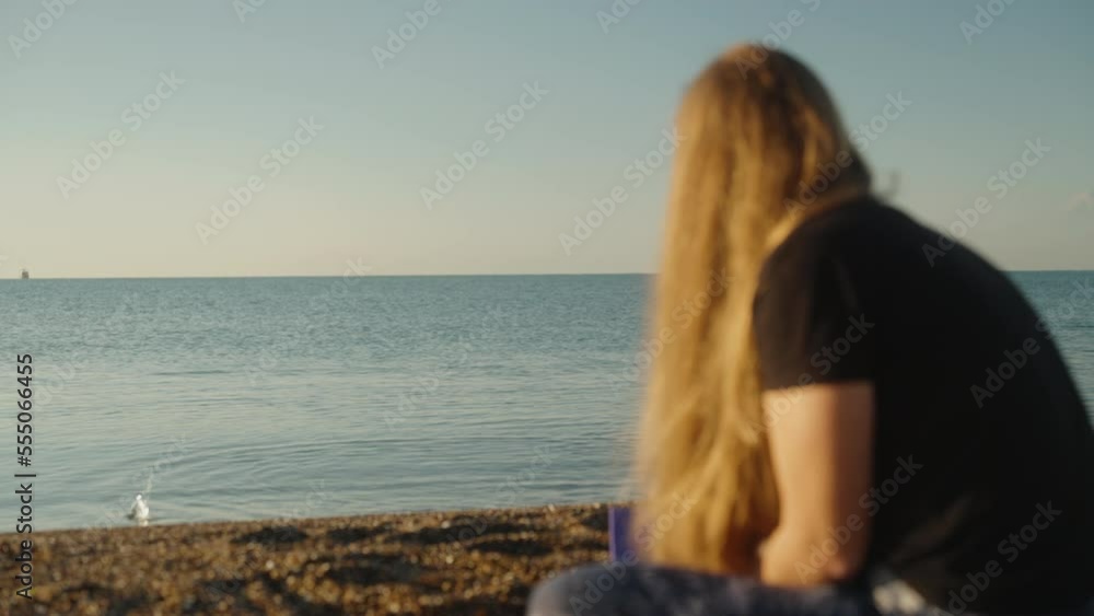 Sunrise on the sea, the sun is still low. The girl sits and throws pebbles into the water so that they jump on the water. Sunrise on the sea, the sun is still low. The girl sits and throws pebbles into the water so that they jump on the water.