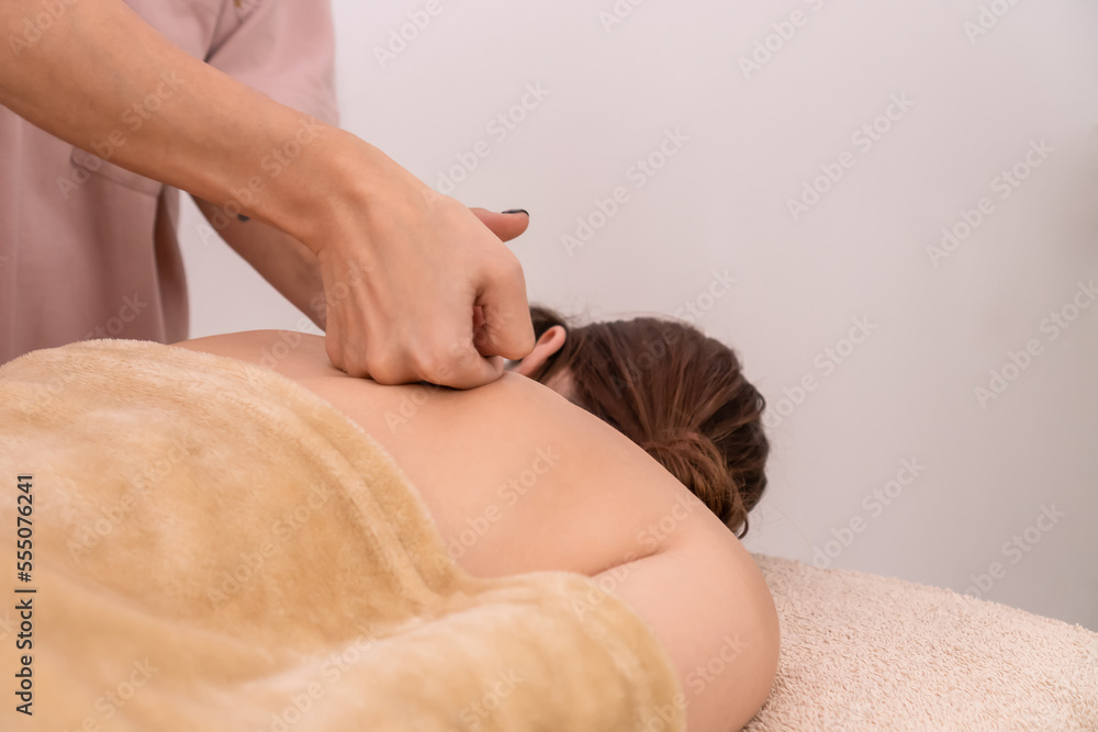 Obraz premium Professional female hands massage the back and shoulder blades of a young brown-haired woman in a spa with soft lighting, close-up. Concept of body care, health, massage spa treatments.