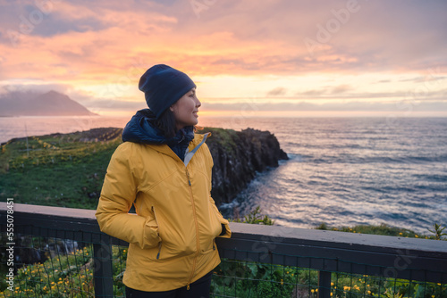 Young asian woman standing and watching puffin bird on the cliff among arctic ocean in Borgarfjordur Eystri on summer at East of Iceland photo