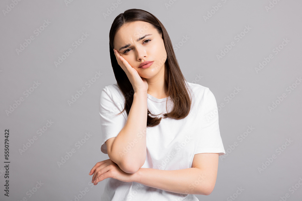 Sad exhausted young girl woman with headache suffering from migraine standing on grey background in studio isolated closing eyes holding arm near head. Sad exhausted young girl woman with headache suffering from migraine standing on grey background in studio isolated closing eyes holding arm near head.