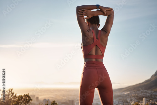 Black woman, fitness and stretching arm on mountain for exercise, workout or training during sunset in outdoors. African American woman in warm up stretch on cliff in sunrise or active life in nature photo