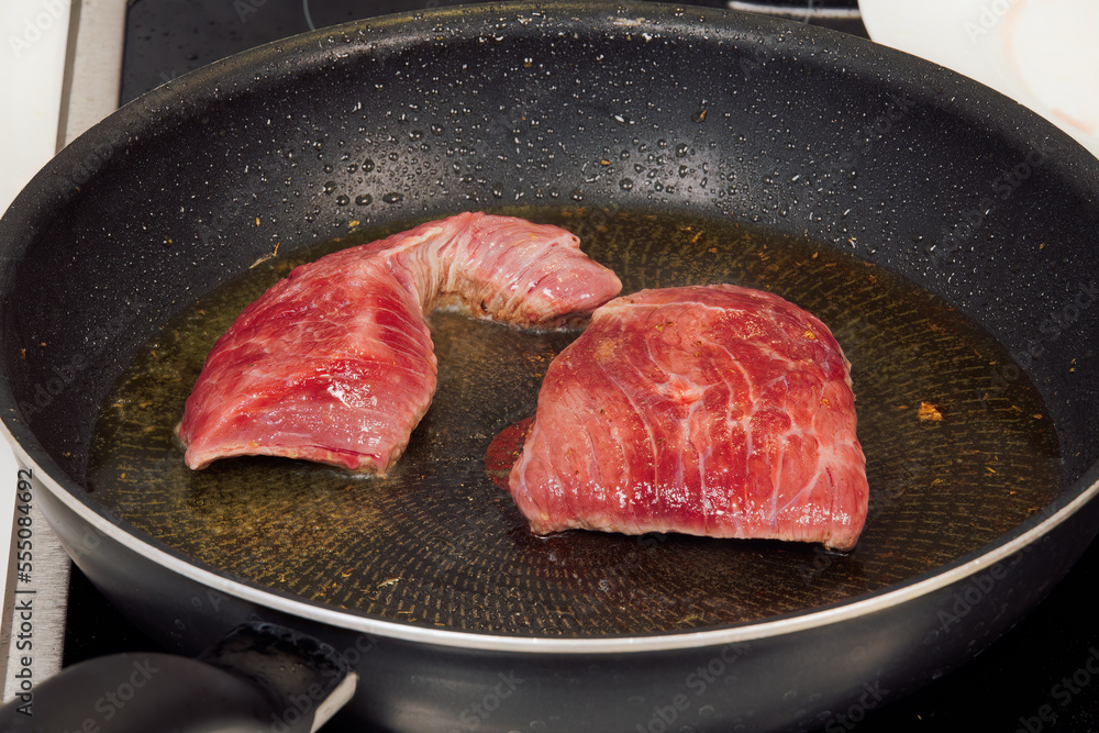 Top sirloin marbled American beef steak kitchen cooking. High-angle focus of raw meat on a hot pan with olive oil.