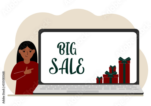 A little girl next to a big laptop, on his screen the text big sales and a lot of gift boxes.