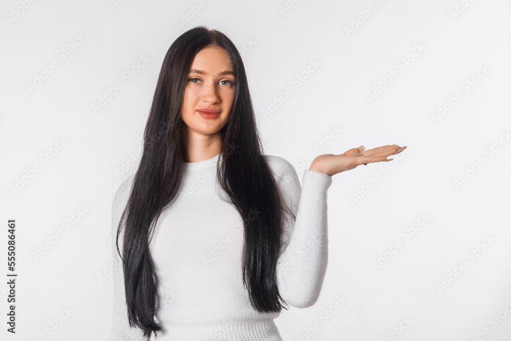 Pleased young brunette woman holding palm open for new product or sale presentation. Happy girl look at the camera, stand over white studio background, copy space for promotion Pleased young brunette woman holding palm open for new product or sale presentation. Happy girl look at the camera, stand over white studio background, copy space for promotion