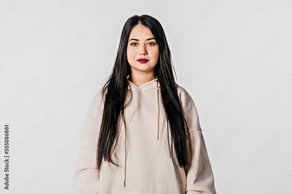 Beautiful pretty lovely girl with long chestnut thick hair and clean glowing facial skin, looking at camera, wear in trendy hoody, standing over white background Beautiful pretty lovely girl with long chestnut thick hair and clean glowing facial skin, looking at camera, wear in trendy hoody, standing over white background