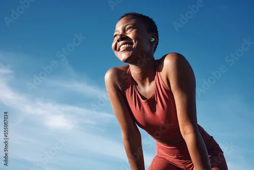 Obraz Fitness, black woman and happy athlete smile after running, exercise and marathon training workout. Blue sky, summer sports and run of a African runner breathing with happiness from sport outdoor