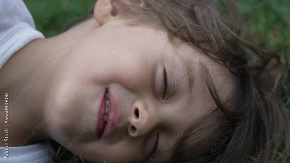 One relaxed child with eyes closed lying on grass at park. Close up happy kid smiling One relaxed child with eyes closed lying on grass at park. Close up happy kid smiling