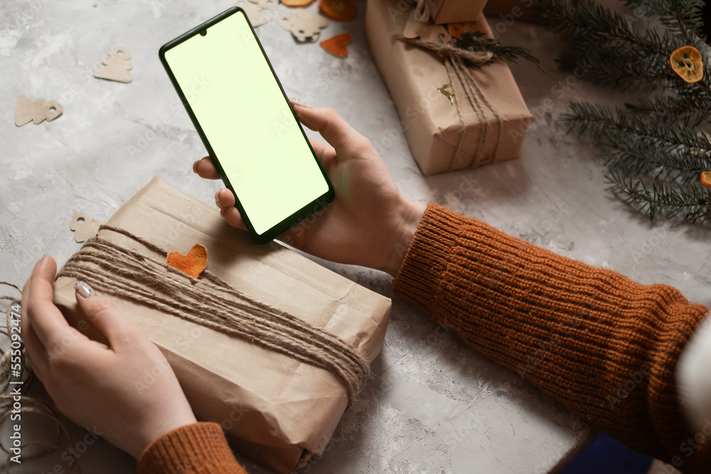 Fototapeta premium a young woman holds a phone, a tablet in her hand and fulfills an order by phone, taking an order for gift wrapping, in the background a Christmas tree and lights