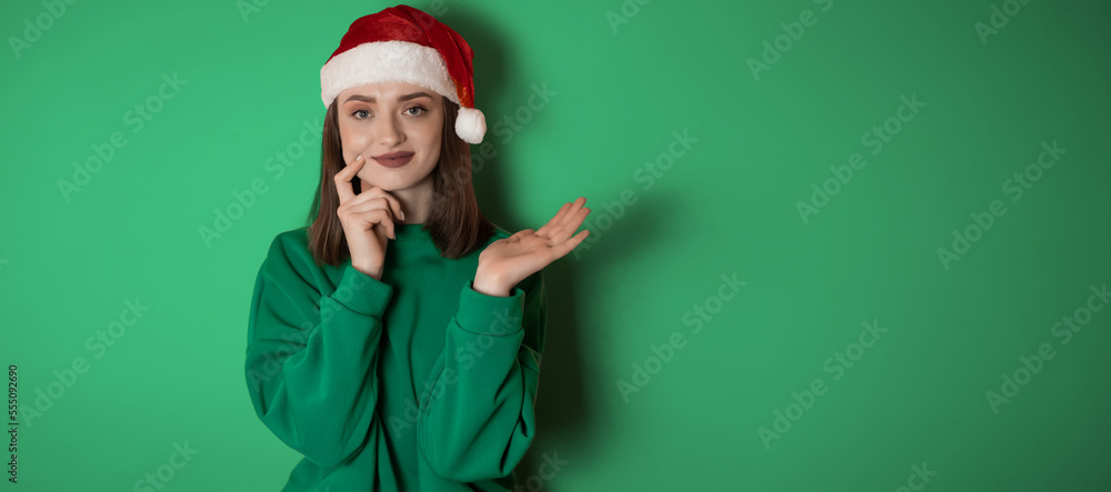Merry surprised young woman wear xmas sweater Santa hat posing pointing hands arms aside indicate on workspace area isolated on plain pastel light green background. Happy New Year 2023 holiday concept Merry surprised young woman wear xmas sweater Santa hat posing pointing hands arms aside indicate on workspace area isolated on plain pastel light green background. Happy New Year 2023 holiday concept