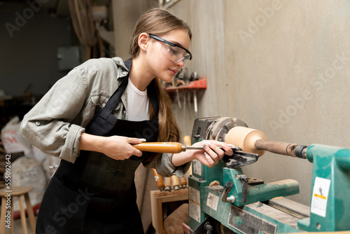 A female carpenter is working at a furniture factory with modern equipment and machinery.