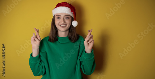 Merry young woman wear xmas sweater Santa hat posing do winner gesture celebrate clenching fists say yes isolated on plain pastel light green background Happy New Year 2023 celebration holiday concept