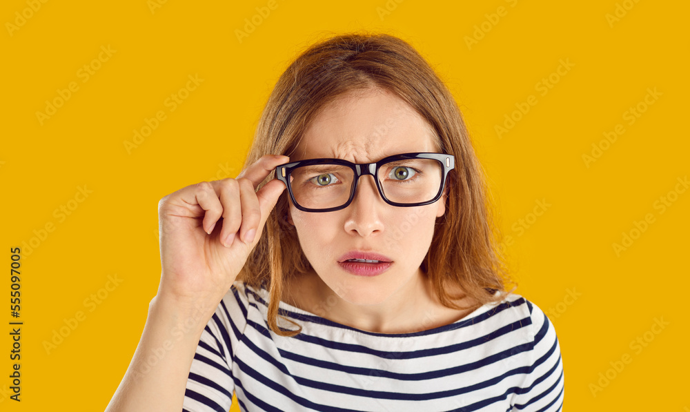 Hey, what did you say. Dissatisfied young woman has focused look and stares at you intently through glasses. Girl who feels disappointed after hearing something unpleasant. Orange background. Hey, what did you say. Dissatisfied young woman has focused look and stares at you intently through glasses. Girl who feels disappointed after hearing something unpleasant. Orange background.