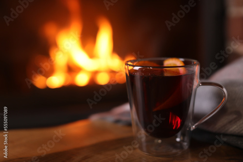 Tasty mulled wine, plaid and blurred fireplace on background