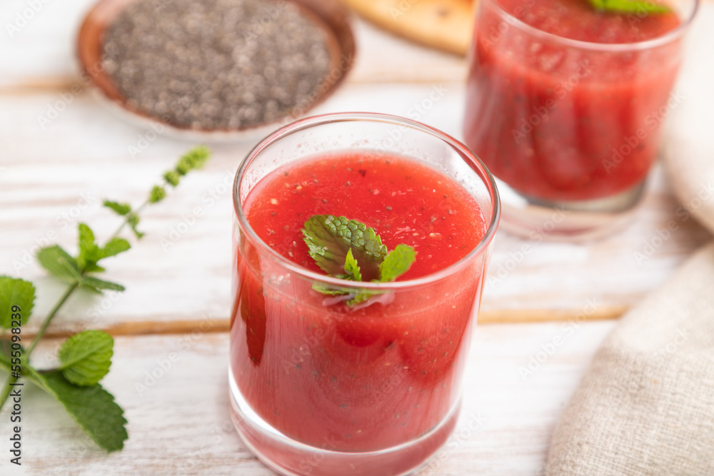 Watermelon juice with chia seeds and mint in glass on a white wooden background with linen textile. Side view, selective focus. Watermelon juice with chia seeds and mint in glass on a white wooden background with linen textile. Side view, selective focus.