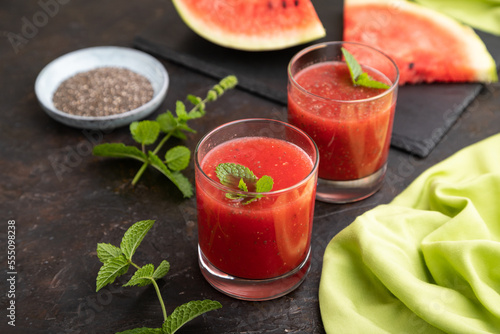 Watermelon juice with chia seeds and mint in glass on a black concrete background with green textile. Side view, selective focus.