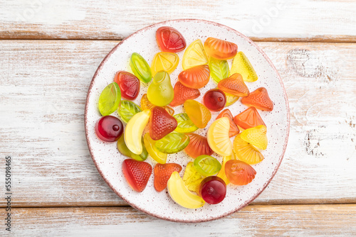 Various fruit candies on plate on white wooden background. close up, top view.