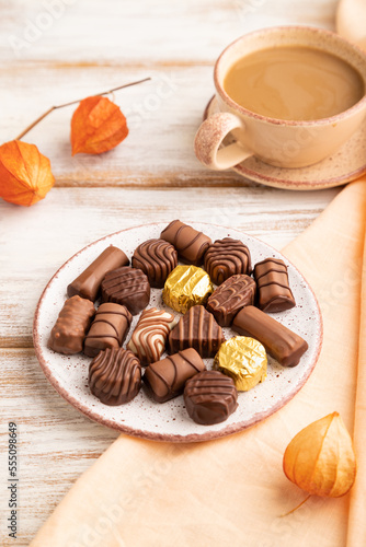 Chocolate candies with cup of coffee and physalis flowers on a white wooden background. side view, close up.