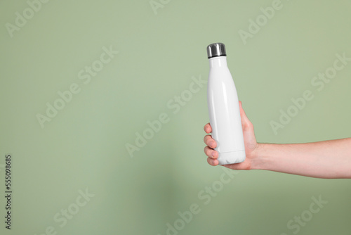 Man holding thermo bottle with drink on olive background, closeup. Space for text