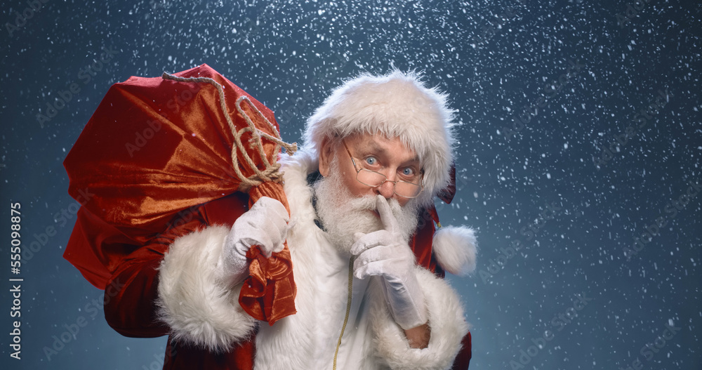 close up portrait of the good old Santa Claus secret hand and lips with a bag of gifts under a snowfall on a red background. Merry Christmas and Happy New Year. Secret Santa close up portrait of the good old Santa Claus secret hand and lips with a bag of gifts under a snowfall on a red background. Merry Christmas and Happy New Year. Secret Santa