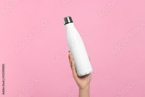 Woman holding thermo bottle on pink background, closeup