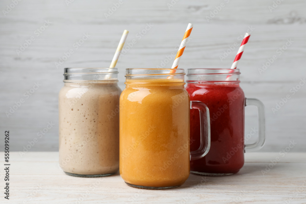 Mason jars with different tasty smoothies on white wooden table Mason jars with different tasty smoothies on white wooden table