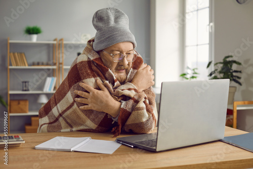 Obraz na płótnie Elderly man in hat sitting at computer wrapped in plaid