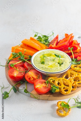 Vegetable tray with green peas and cream cheese dip on a light concrete background. Vegetarian recipes.
