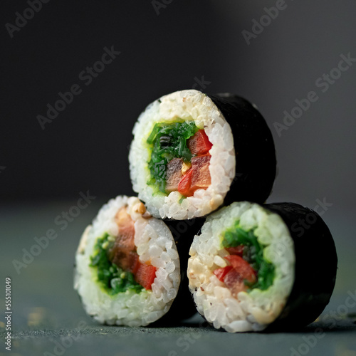 Pyramid of three sushi rolls. Vegetarian sushi rolls with green onions and red peppers. Fitness rolls. Low calorie meal. Healthy food. Side view. Close-up. Soft focus. Dark background with backlight.